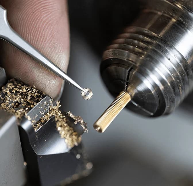 A small component held in tweezers beside a lathe